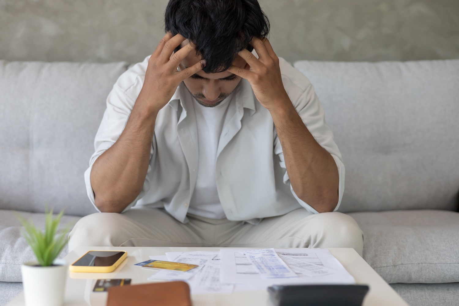 A man staring at his bills with his credit card and phone beside him
