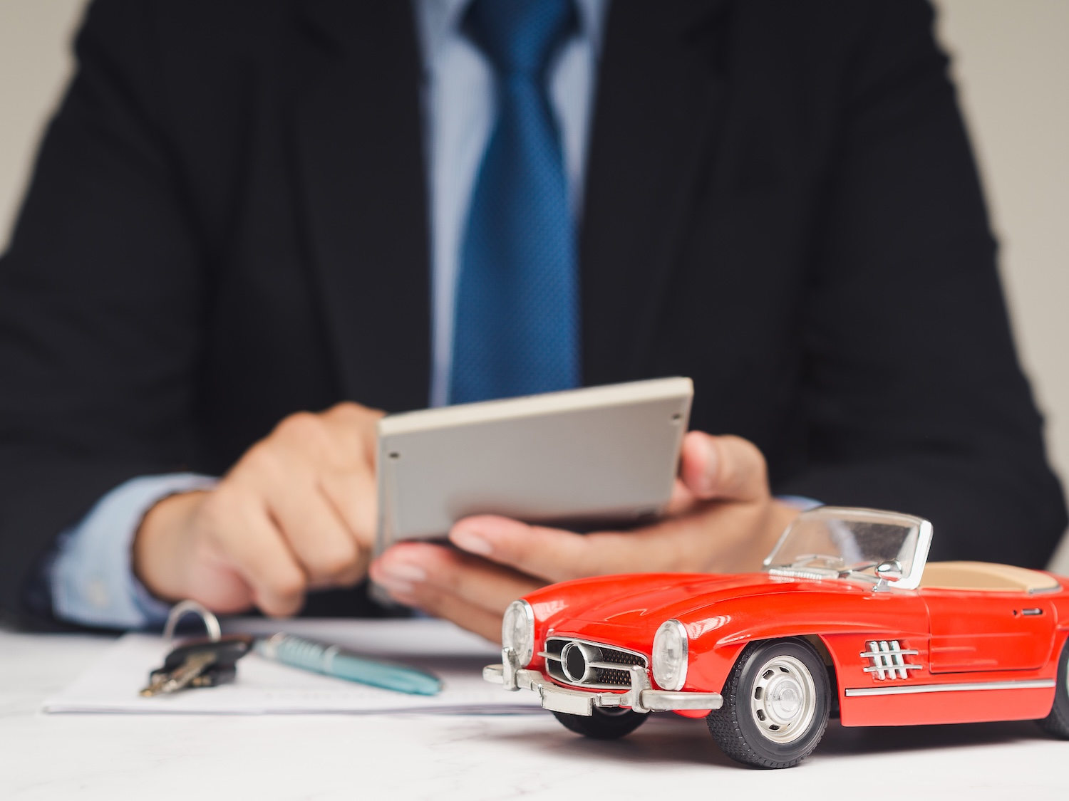 Man in a suit on a calculator looking for help with logbook loans debt. He has a set of car keys and a red model car in front of him.