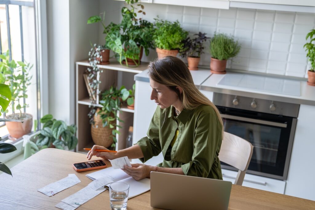 Lady sat at table with calculator, laptop and bills looking at high-cross credit and how to get out when interest is working against you